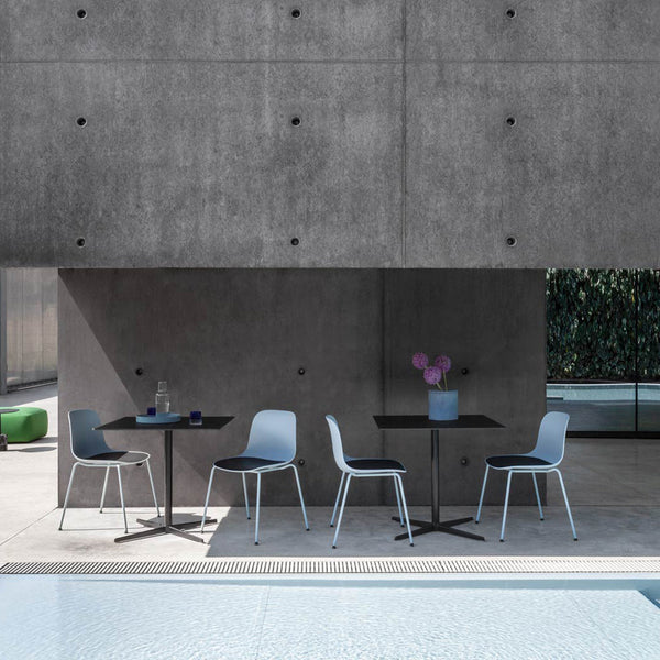 Stylish outdoor dining set featuring light blue chairs, a sleek black table, and a floral centerpiece against a concrete backdrop.