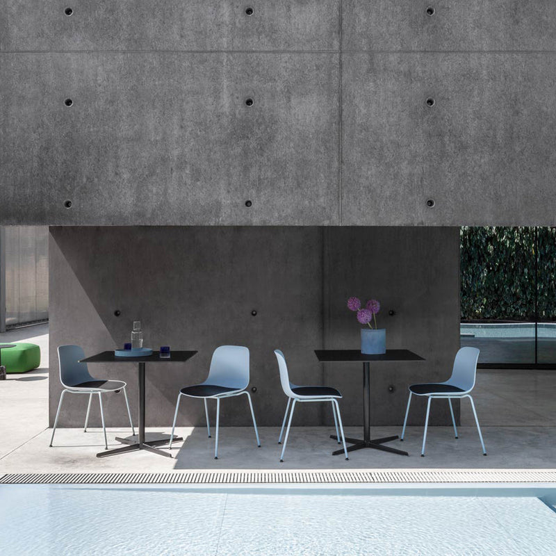 Stylish outdoor dining set featuring light blue chairs, a sleek black table, and a floral centerpiece against a concrete backdrop.