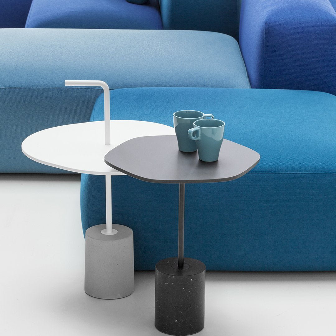Modern side tables in white and black, featuring sleek designs and textured grey bases, against a vibrant blue backdrop.