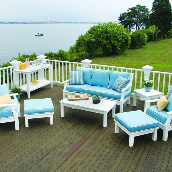 Light blue cushions on white patio furniture, set against a lush green landscape and calm water backdrop.