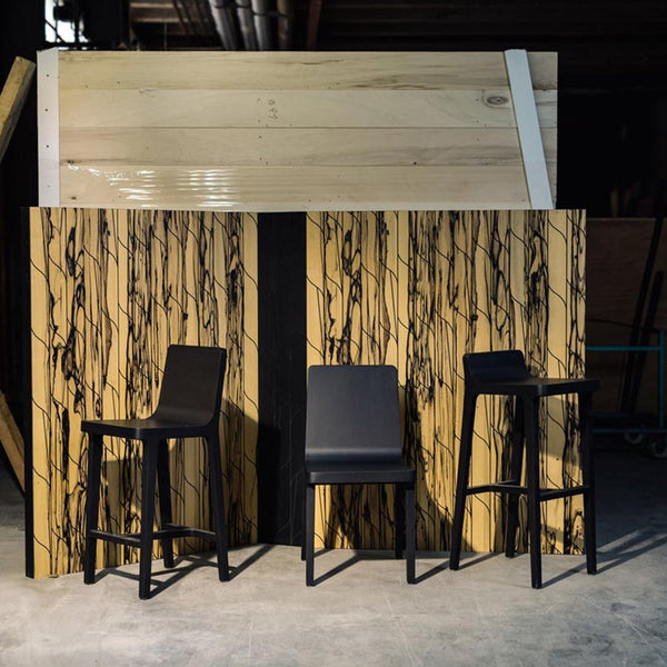 "Modern bar stools with sleek black finish against a striking, patterned wood backdrop in warm tones."