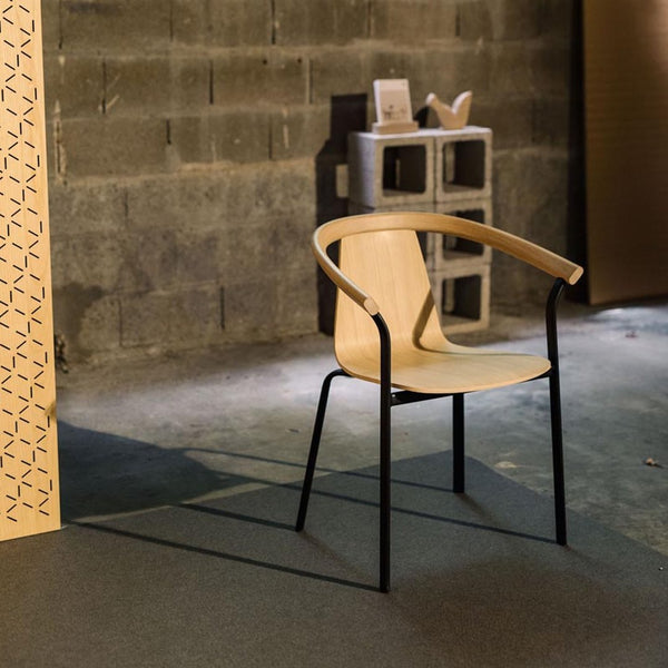 Light wood chair with black metal legs, featuring a minimalist design against a textured concrete background.