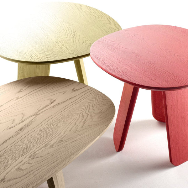 Three round tables in soft green, warm beige, and vibrant red finishes with textured wood grain patterns.