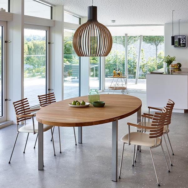 Elegant wooden oval dining table with metal legs, surrounded by striped wood and beige chairs, in a bright, airy space.