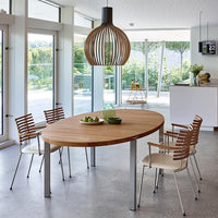 Elegant wooden oval dining table with metal legs, surrounded by striped wood and beige chairs, in a bright, airy space.