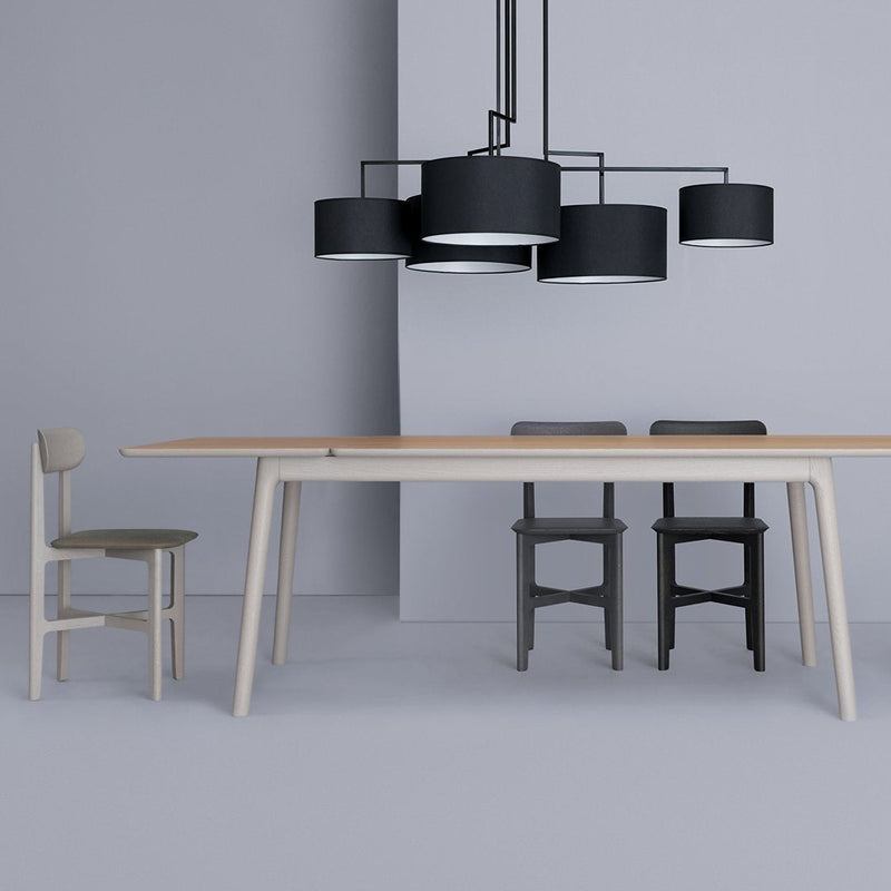Modern dining setup featuring a light wood table, gray chairs, and black pendant lights against a soft gray backdrop.