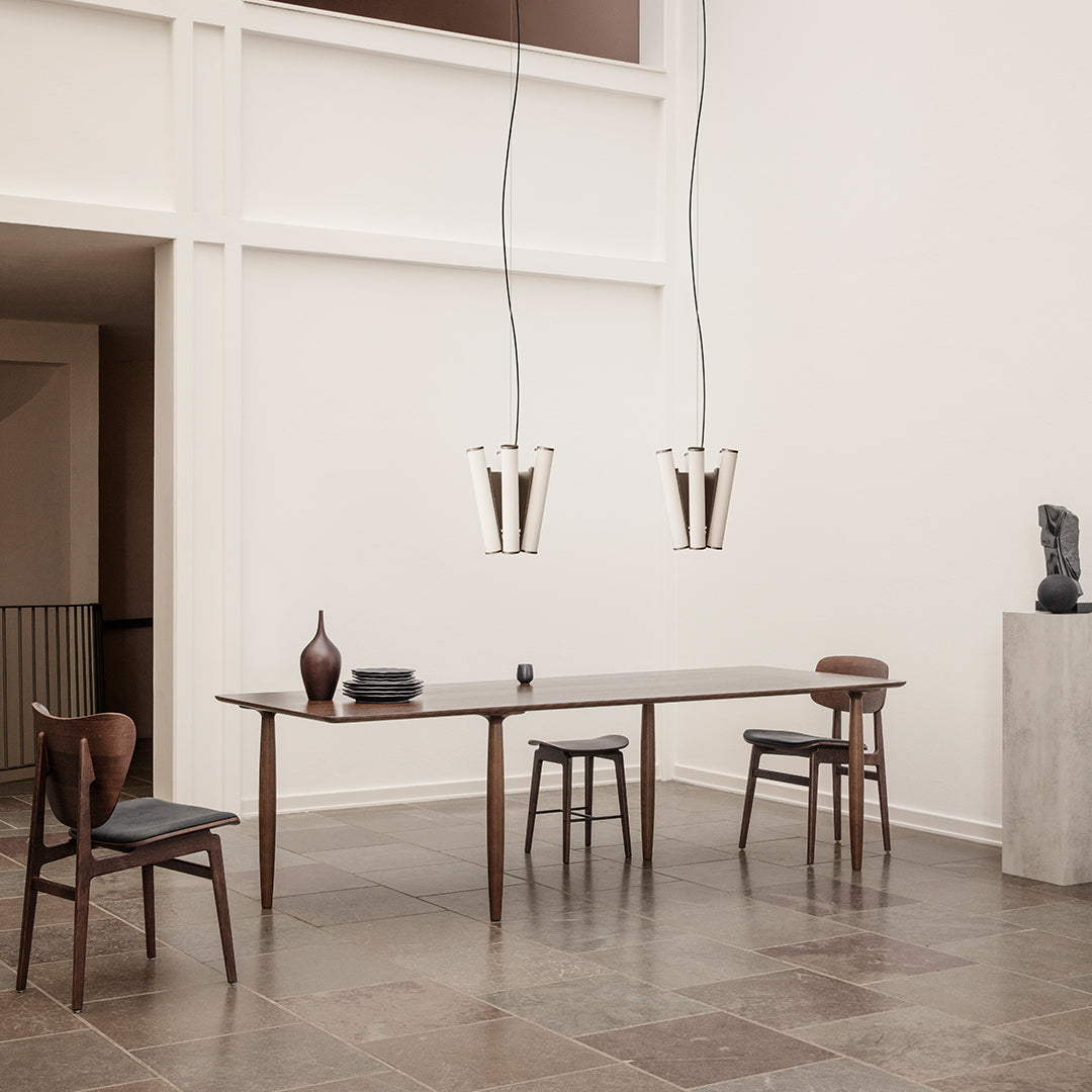 Modern dining room featuring a dark wood table, light wooden chairs, and sleek, minimalistic pendant lights in warm tones.