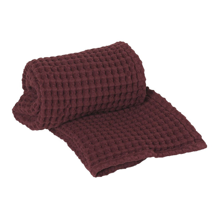 Burgundy waffle-patterned blanket, rolled and partially unrolled, showcasing rich texture and deep color.