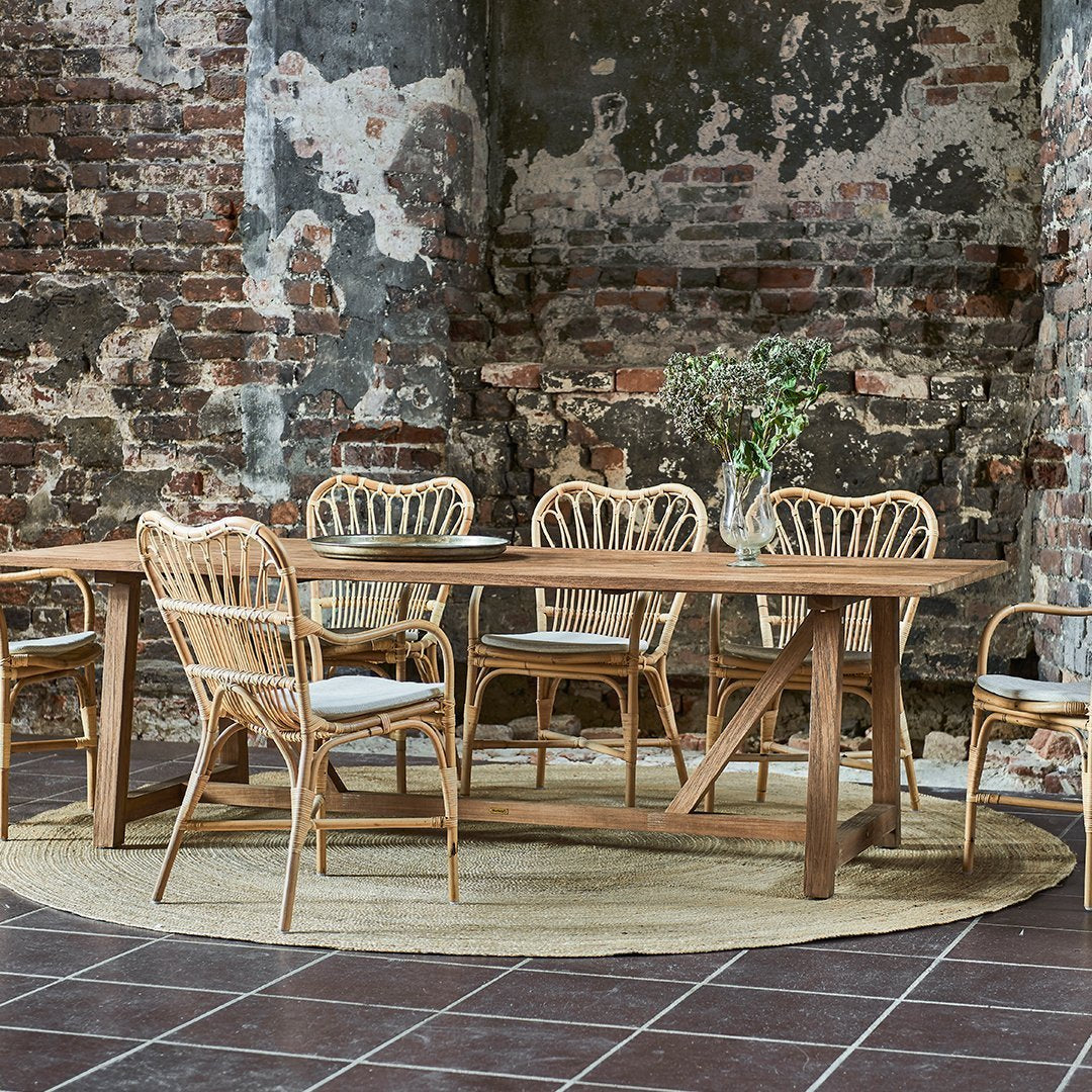 Light brown wooden dining table with rattan chairs, complemented by natural tones and textures in a rustic setting.