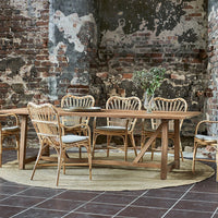 Light brown wooden dining table with rattan chairs, complemented by natural tones and textures in a rustic setting.