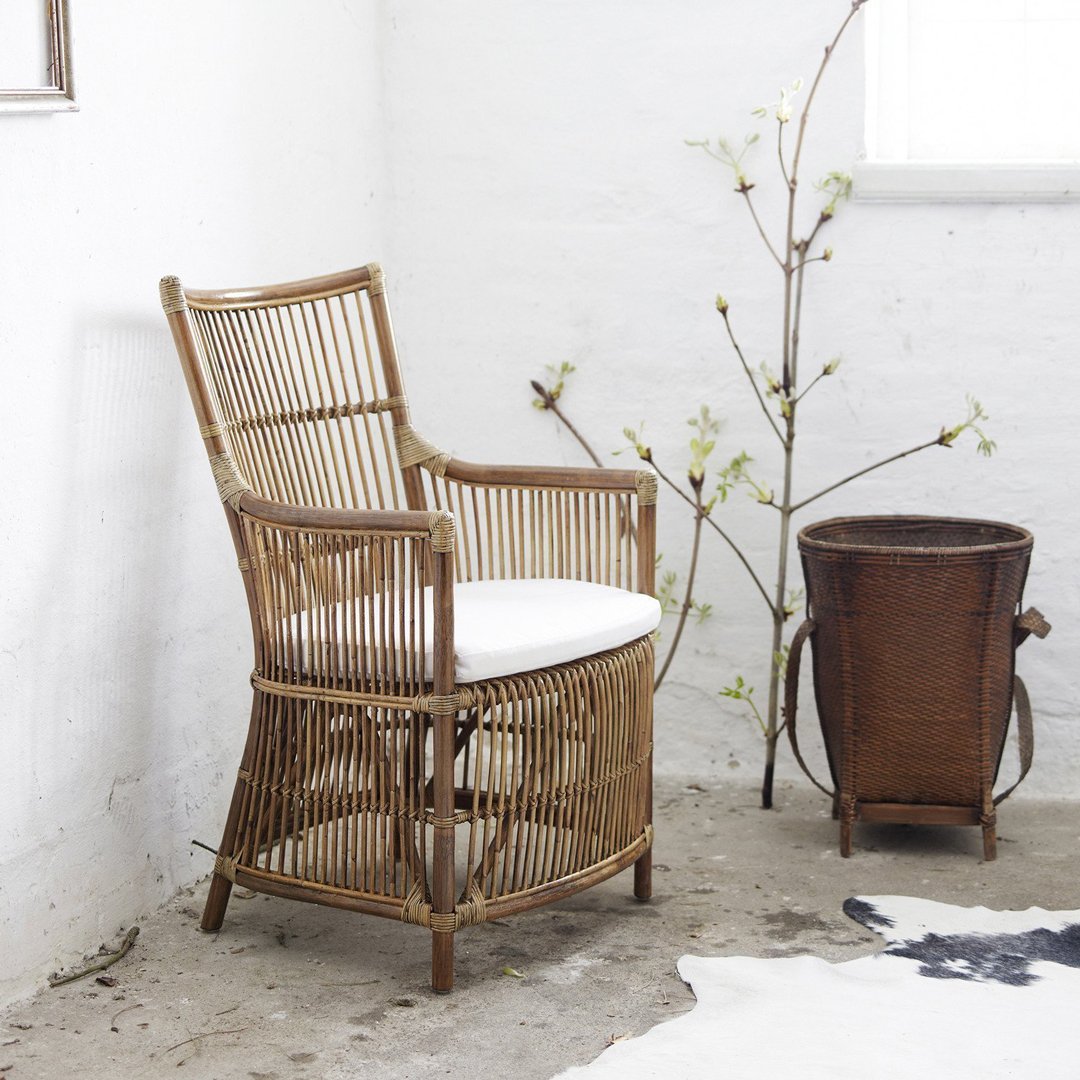 Rattan chair with natural bamboo hues and a white cushion, paired with a brown basket and minimalist decor.
