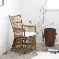 Rattan chair with natural bamboo hues and a white cushion, paired with a brown basket and minimalist decor.