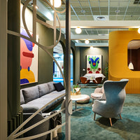 "Modern seating area with muted gray sofa, vibrant abstract artwork, and teal carpet for a stylish pop of color."