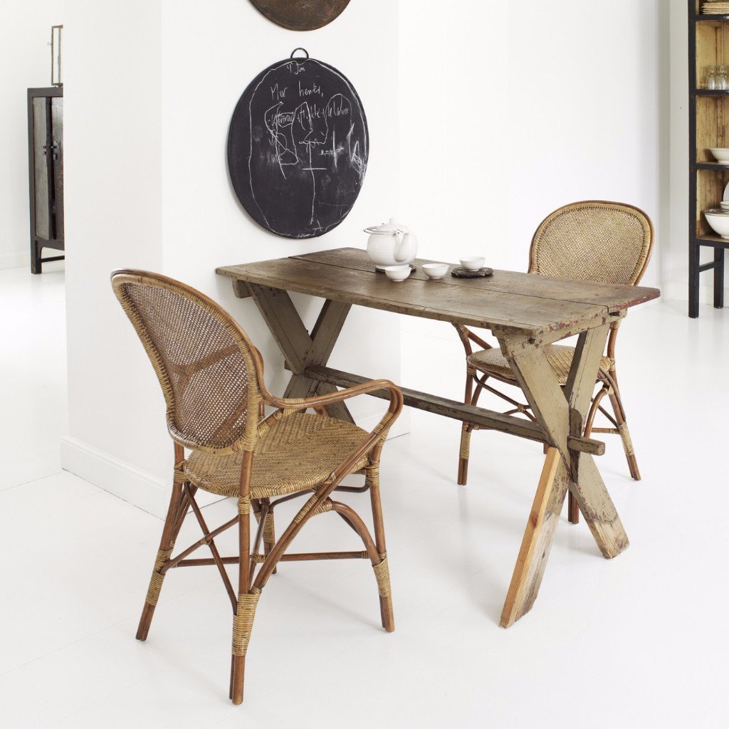 Rustic wooden table with natural tones, paired with woven rattan chairs featuring neutral and earthy patterns.
