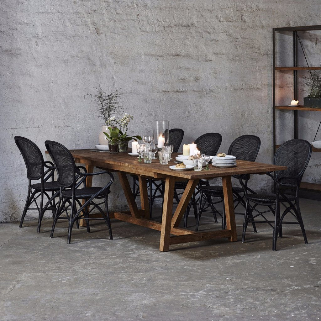 Rustic wooden dining table with dark wicker chairs, featuring natural textures and earthy tones. Perfect for modern decor.