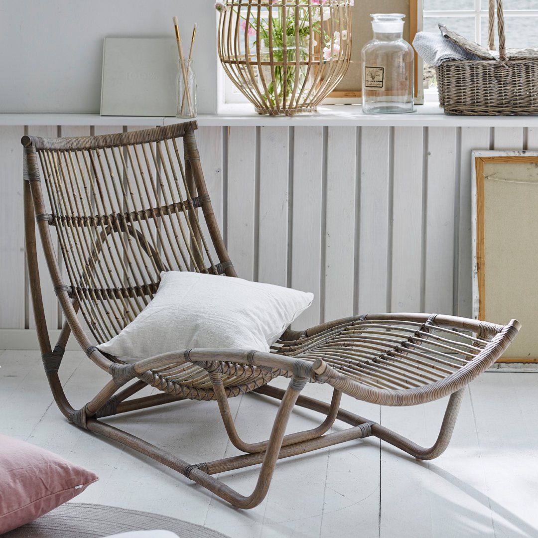 "Light brown rattan chair with curved lines, textured patterns, and a white pillow, set against a bright interior."
