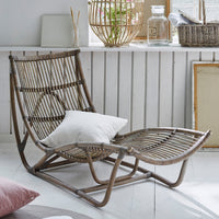 "Light brown rattan chair with curved lines, textured patterns, and a white pillow, set against a bright interior."