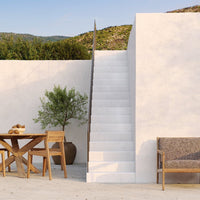 White staircase against textured beige walls, with natural wood accents and greenery in a serene outdoor setting.