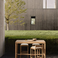 Natural wood table and chairs in neutral tones, set against a modern grey wooden backdrop and lush green grass.