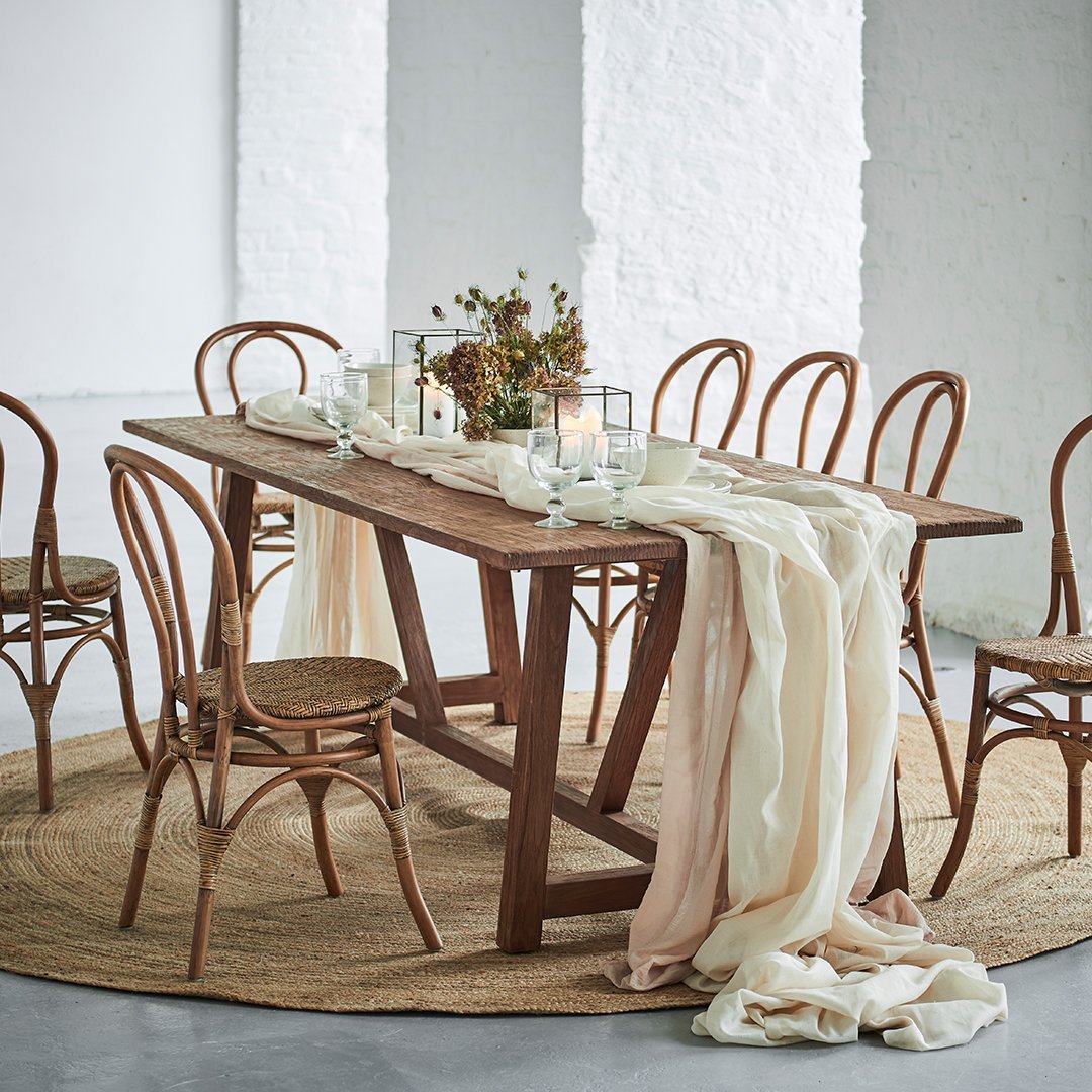 "Natural wood table with neutral tones, soft cream drapes, and woven beige rug, accented by clear glass decor."