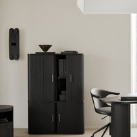 Black cabinet with vertical grooves, gold accents, set against a neutral wall with minimalistic decor.