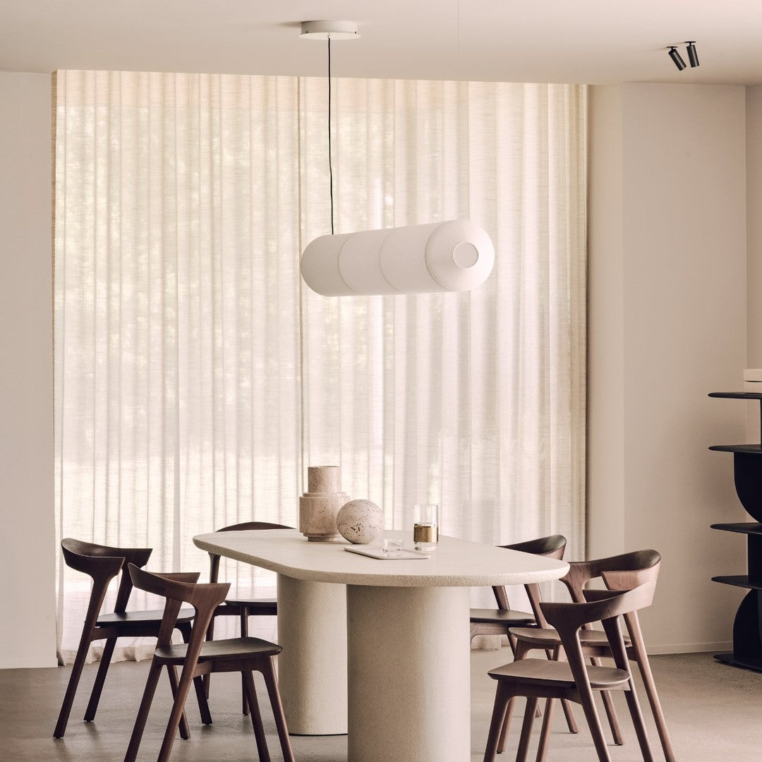 Modern white pendant lamp above a round stone table, set against soft beige curtains and dark wooden chairs.