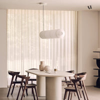 Modern white pendant lamp above a round stone table, set against soft beige curtains and dark wooden chairs.