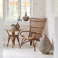 "Natural rattan chair and table set with neutral tones and subtle floral patterns on a light wall."