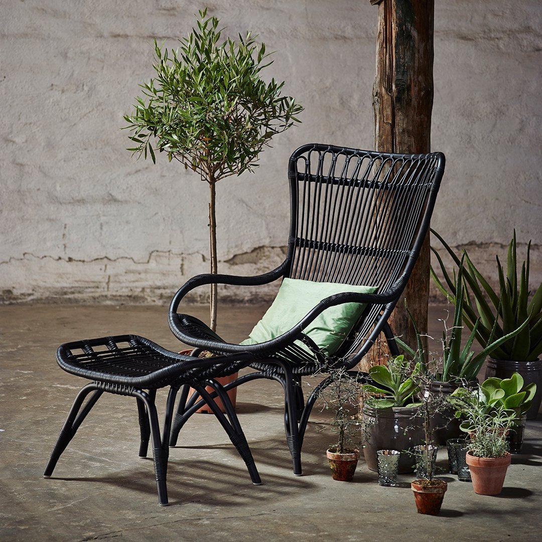 Black woven chair with matching footrest, featuring a light green cushion against a neutral background.