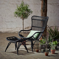 Black woven chair with matching footrest, featuring a light green cushion against a neutral background.