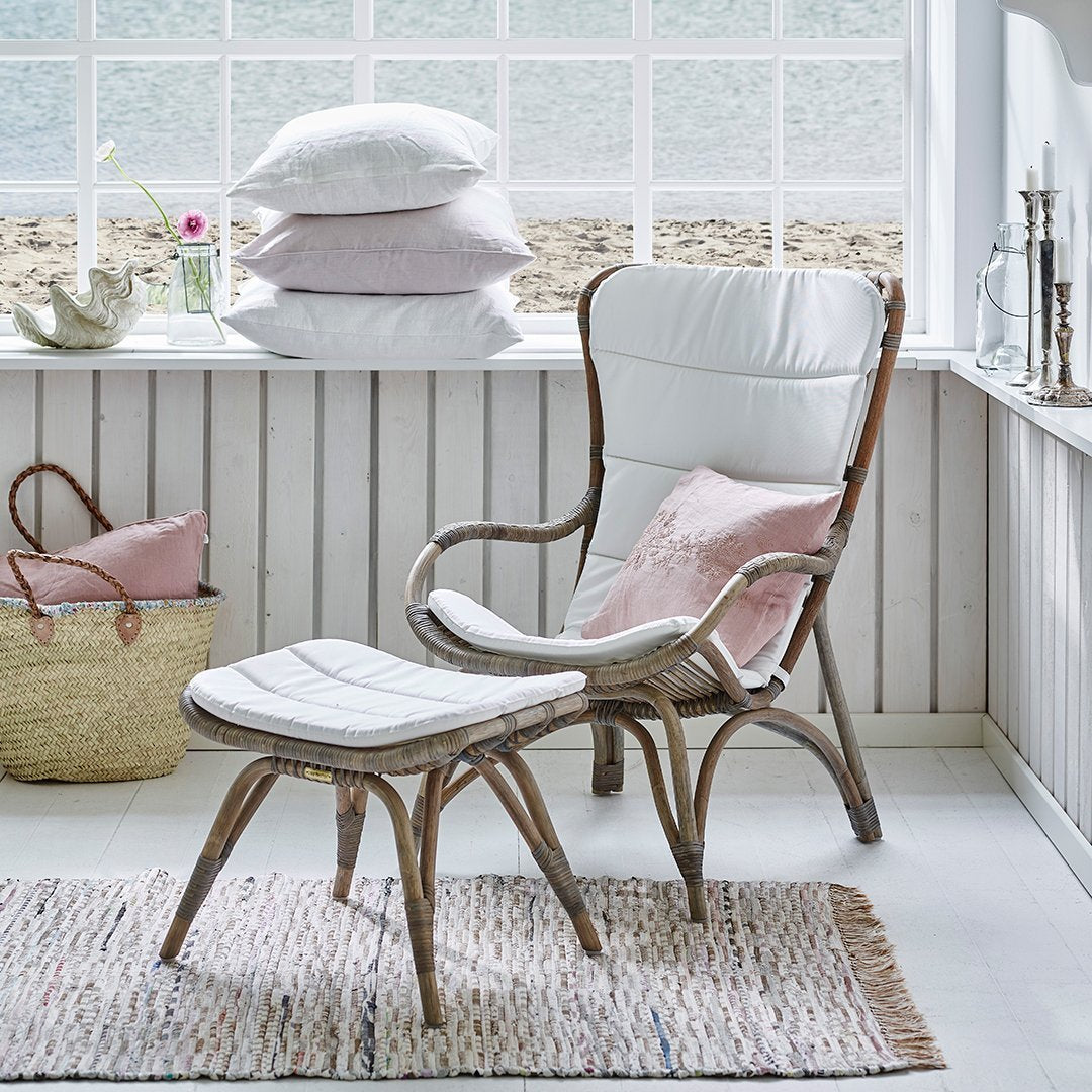 White wicker chair with light pink cushions, complemented by a textured beige rug and soft pastel decor.