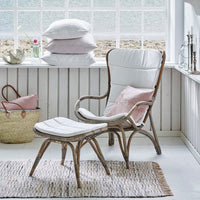 White wicker chair with light pink cushions, complemented by a textured beige rug and soft pastel decor.