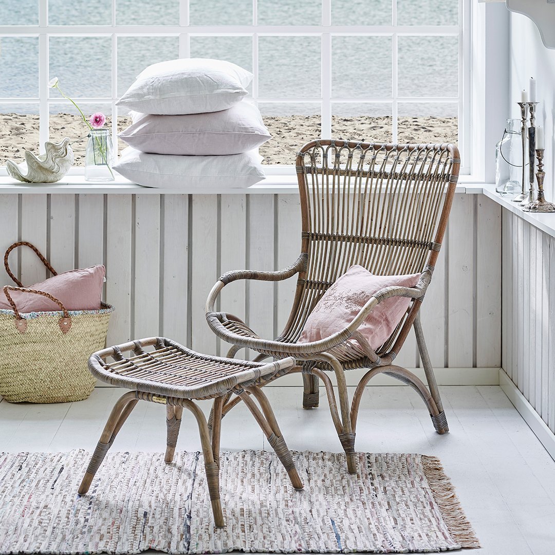 "Natural woven rattan chair and ottoman with soft pink cushions, set against a light, airy white decor."