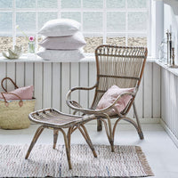 "Natural woven rattan chair and ottoman with soft pink cushions, set against a light, airy white decor."