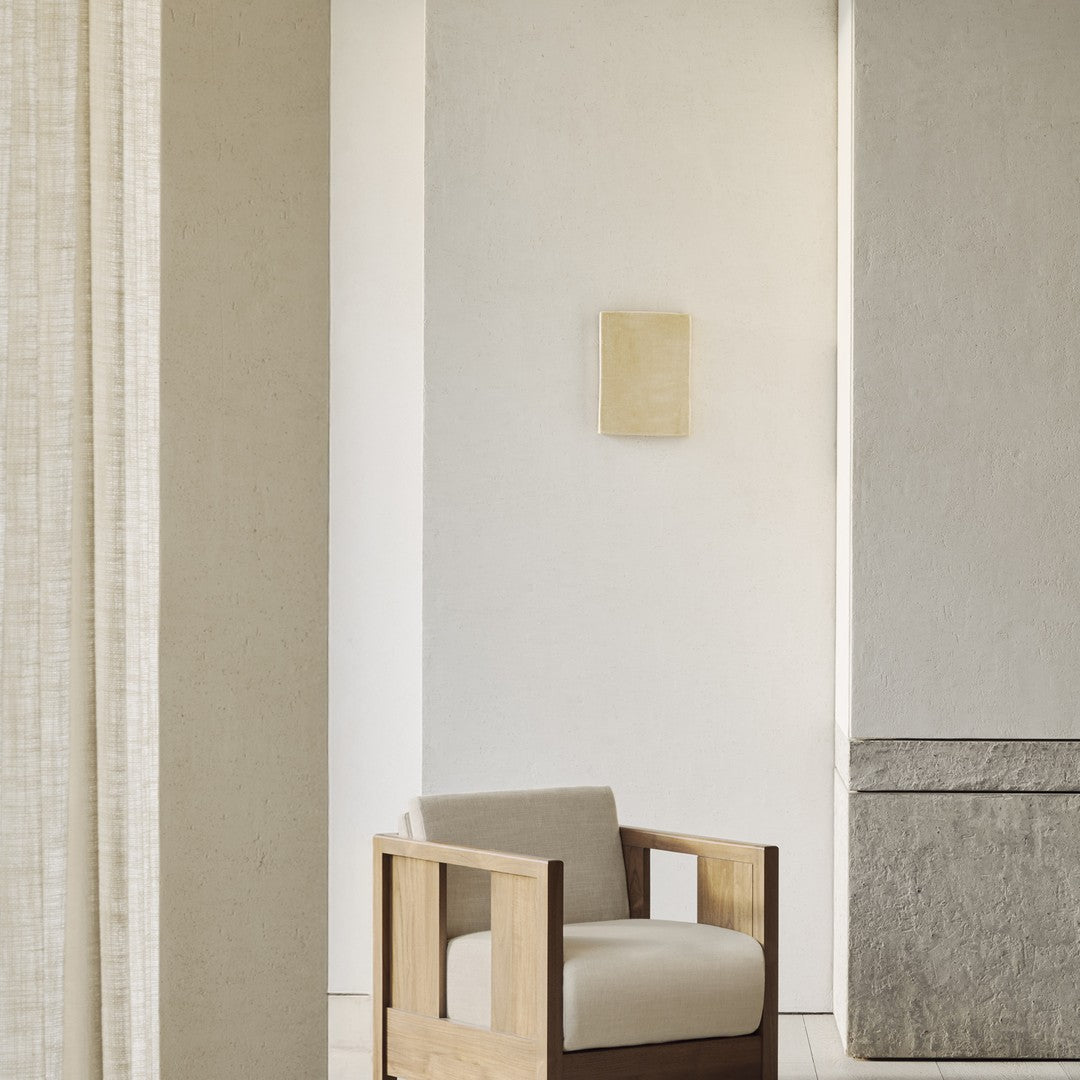 Neutral beige armchair with a simple, clean design against a light, textured wall and soft, muted decor.