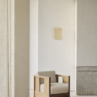 Neutral beige armchair with a simple, clean design against a light, textured wall and soft, muted decor.