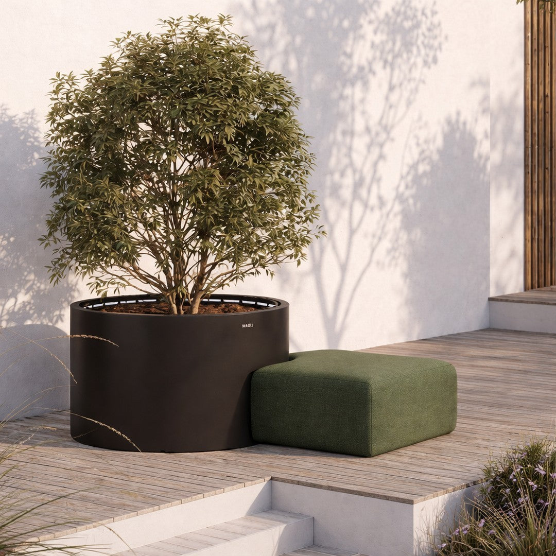 Black round planter with vibrant green foliage and a textured green ottoman on a wooden deck.