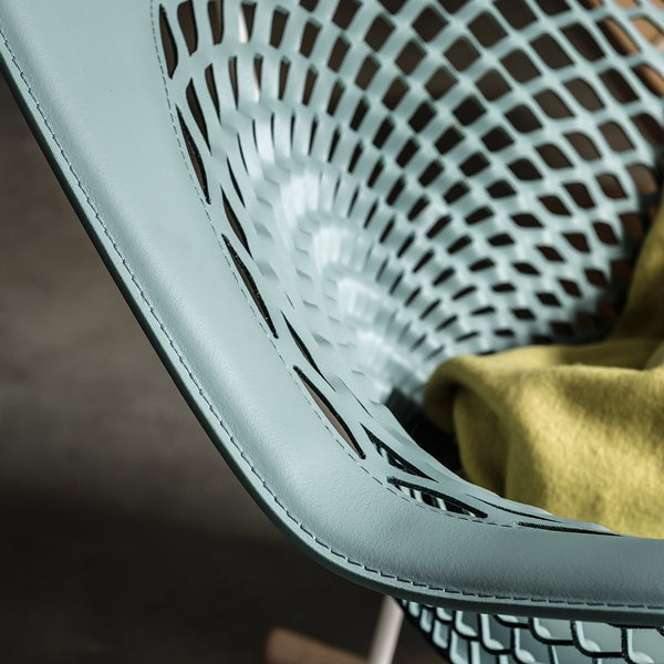 Blue mesh chair detail with a modern pattern, featuring a vibrant green throw draped over for contrast.