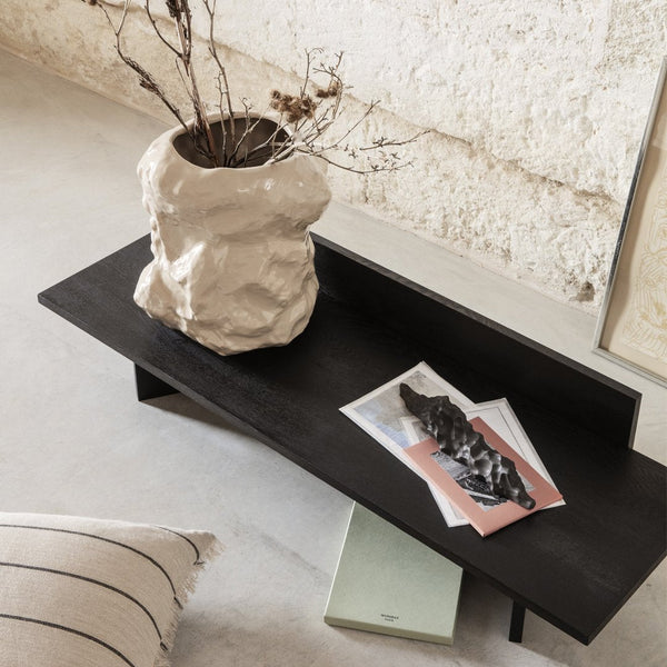 Black minimalist coffee table featuring a textured beige vase and layered pastel papers on a neutral background.