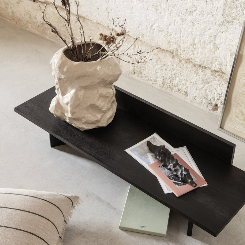 Black minimalist coffee table featuring a textured beige vase and layered pastel papers on a neutral background.