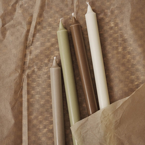 "Set of four tapered candles in earthy tones: olive green, brown, cream, and white on textured brown paper."