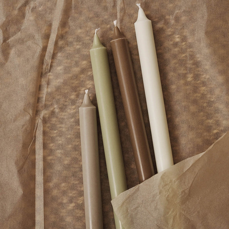 "Set of four tapered candles in earthy tones: olive green, brown, cream, and white on textured brown paper."