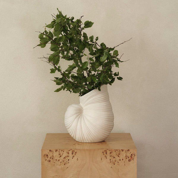 White textured vase with a spiral design, showcasing vibrant green foliage, on a natural wood pedestal.