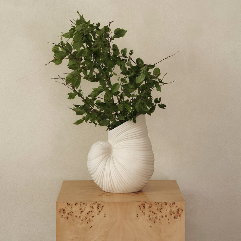 White textured vase with a spiral design, showcasing vibrant green foliage, on a natural wood pedestal.