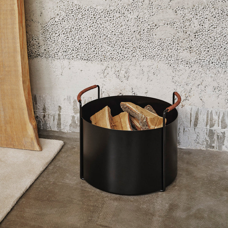 Stylish black metal log holder with tan leather handles, featuring a smooth, minimalist design.
