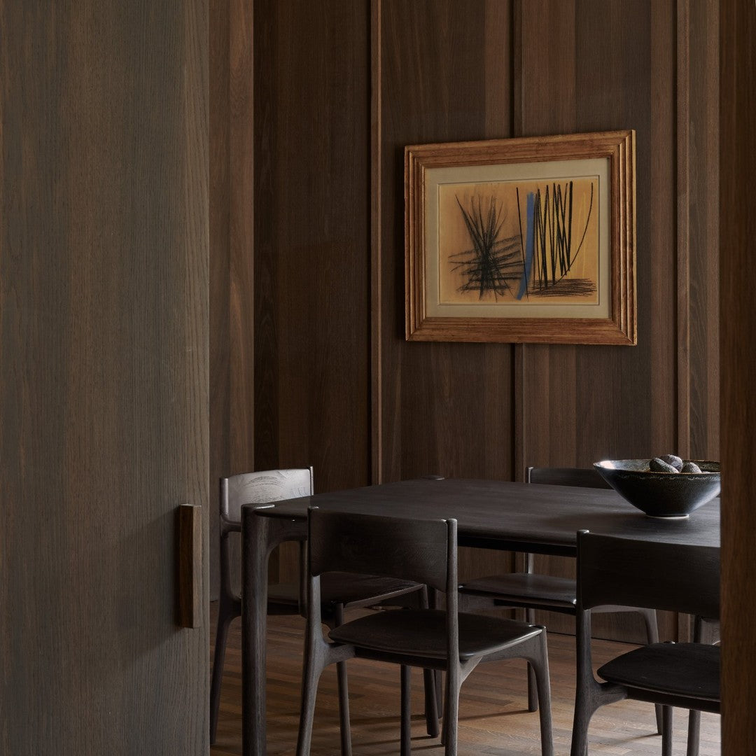 "Dark wood tones with a subtle grain pattern, featuring black chairs and a bowl of smooth stones against a warm, earthy backdrop."