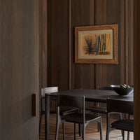 "Dark wood tones with a subtle grain pattern, featuring black chairs and a bowl of smooth stones against a warm, earthy backdrop."