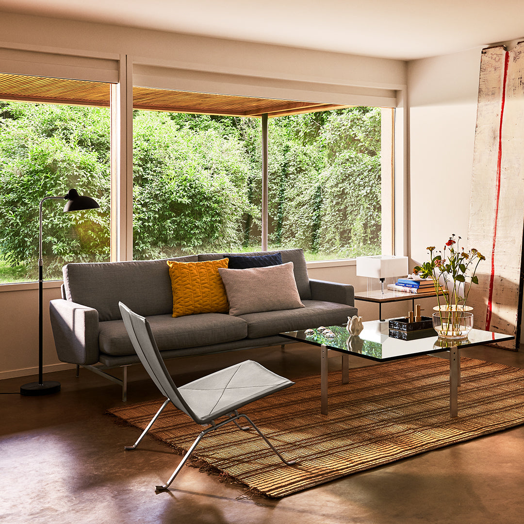 Modern living room featuring a gray sofa, yellow accent pillow, glass coffee table, and a striped rug in neutral tones.