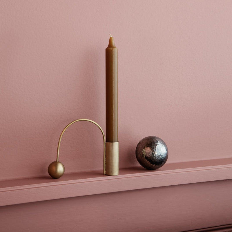 Brown candle holder with a gold accent, against a soft pink backdrop, complemented by a shiny black sphere.