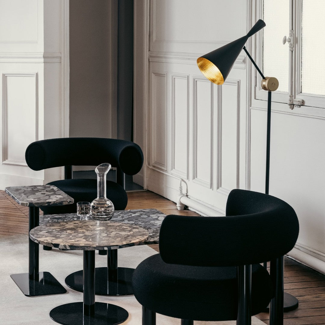 Black upholstered chairs and marble tables with sleek, modern patterns, complemented by a stylish black and gold lamp.